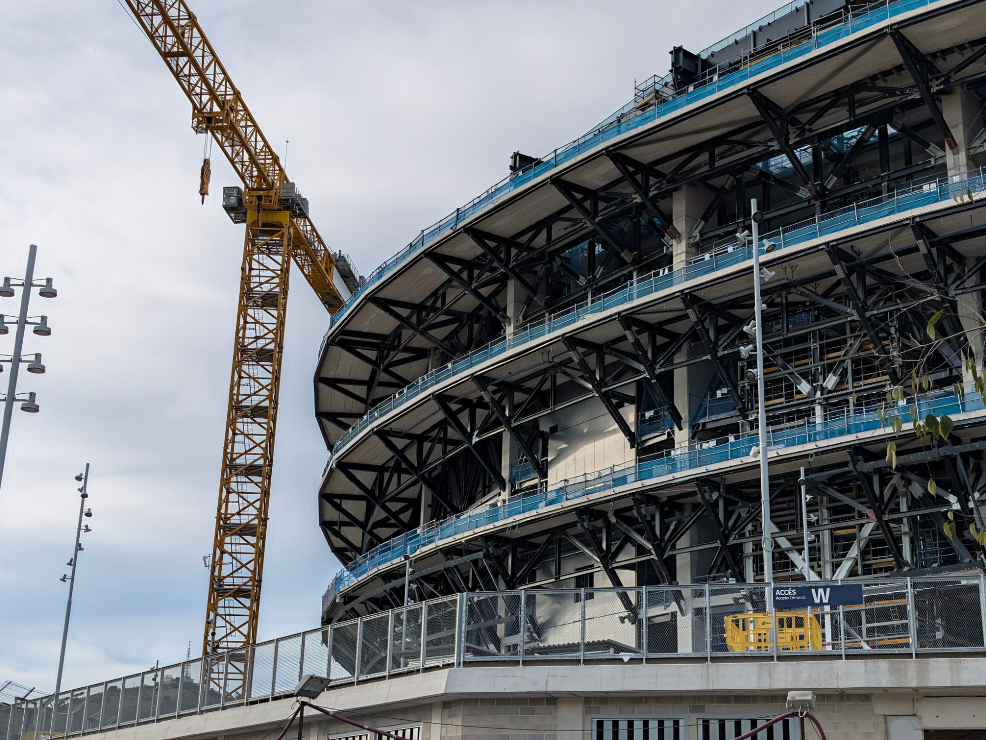 Steel trusses and concrete decks of a stadium under construction, with a tower crane
